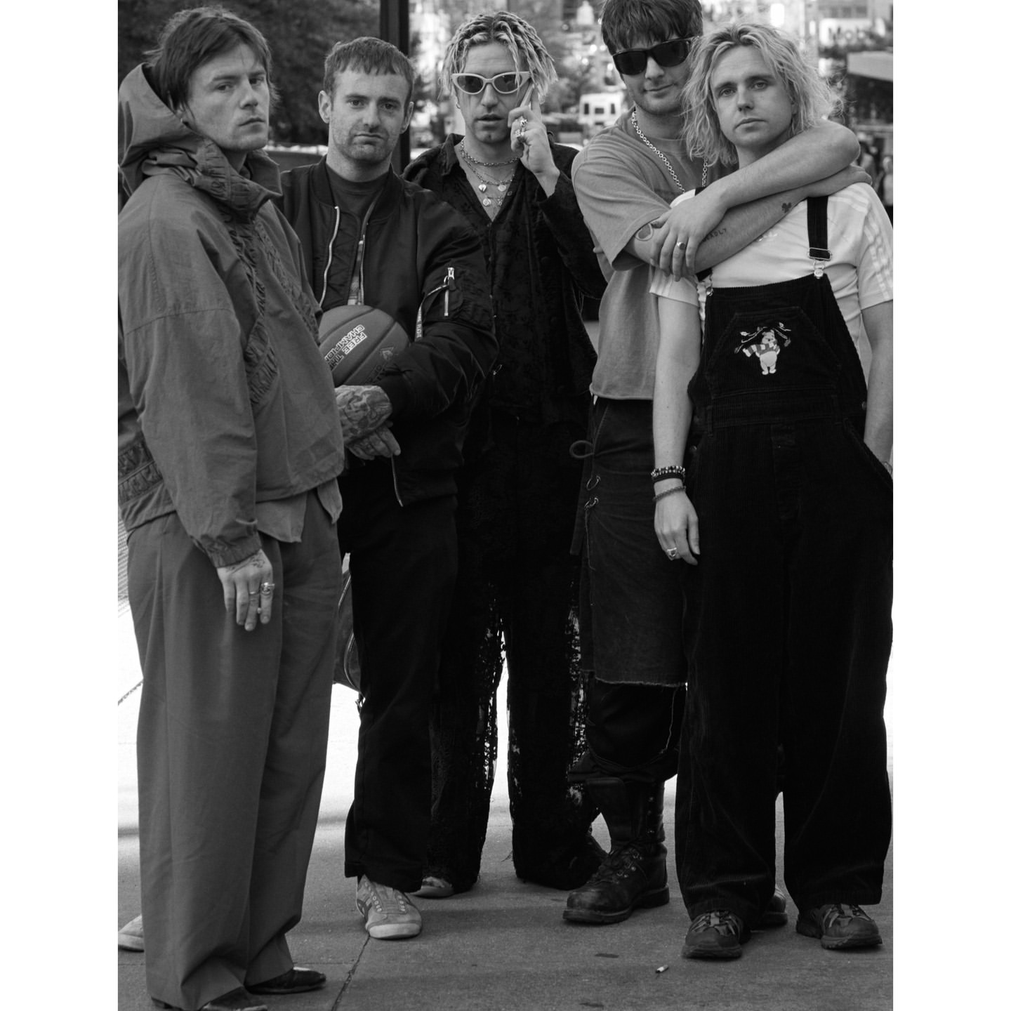 Black-and-white portrait of five adult men in casual attire standing outdoors in daylight, showcasing urban fashion and a group dynamic.