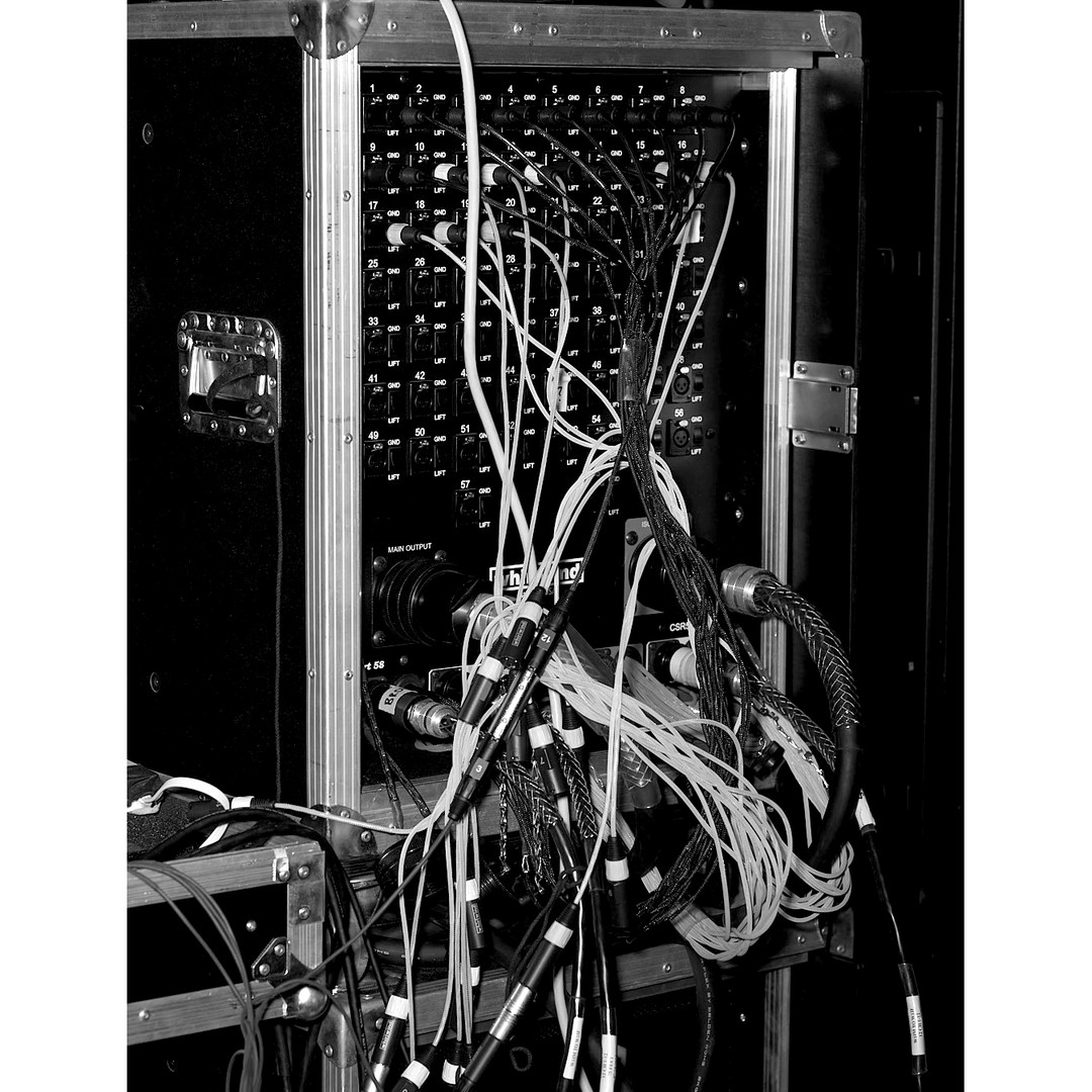 Black and white photograph showcases a complex array of audio cables connected to a rack-mounted audio patch panel in a studio setting.