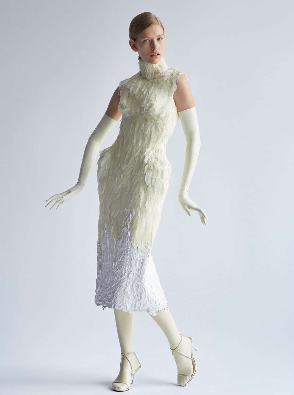 Fashion model in studio wearing a white feather dress, gloves, and high heels. Full-length shot on white background, high fashion.