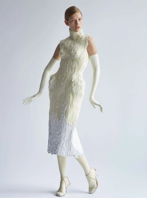 Fashion model in studio wearing a white feather dress, gloves, and high heels. Full-length shot on white background, high fashion.