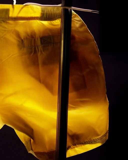 Close-up of yellow swim trunks on a black metal rack with a white drawstring, set against a dark background.