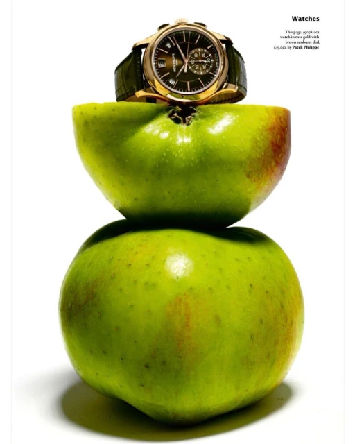 Wristwatch with a green leather band is displayed on top of stacked green apple halves against a clean, white backdrop in a studio shot.