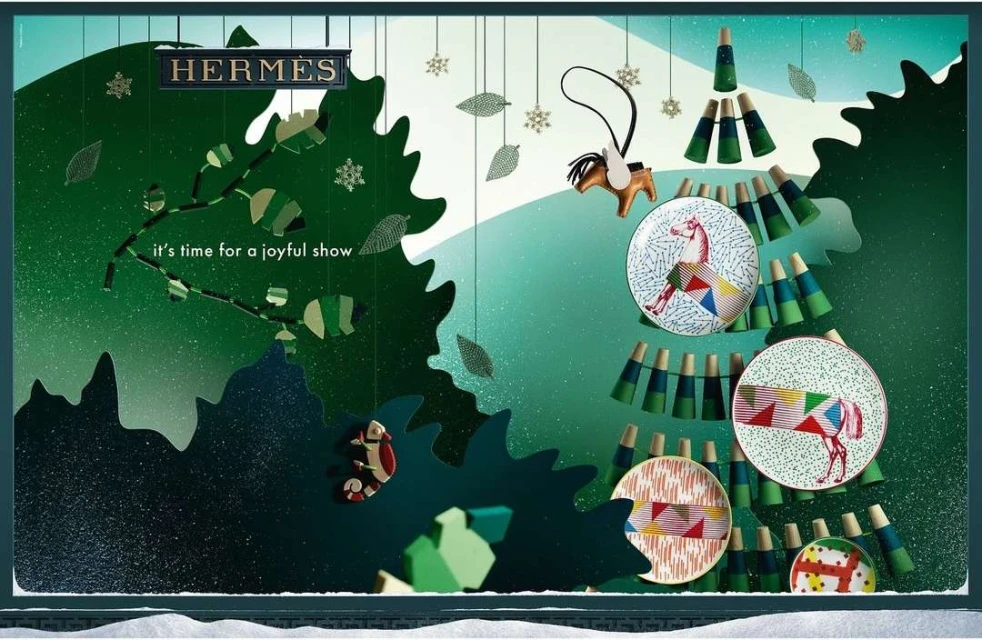 Holiday window display for Hermès featuring a Christmas tree made from plates and miniature painted wood objects, festive and elegant.