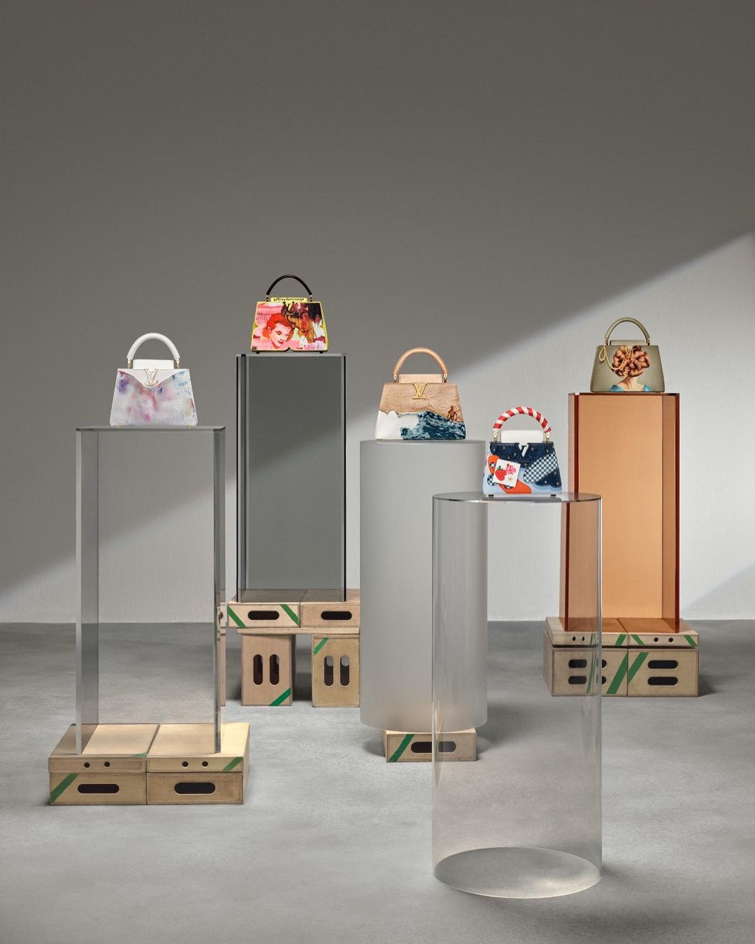 Arrangement of luxury handbags displayed on transparent acrylic and wooden podiums in a minimalist studio setting with neutral background.