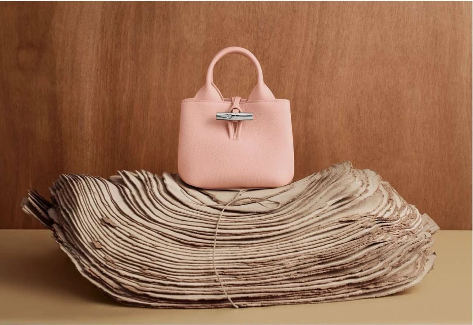 Stylish pink leather handbag on sculpted paper against a wood backdrop. Fashion product shot with luxury feel, studio lighting, and clean style.