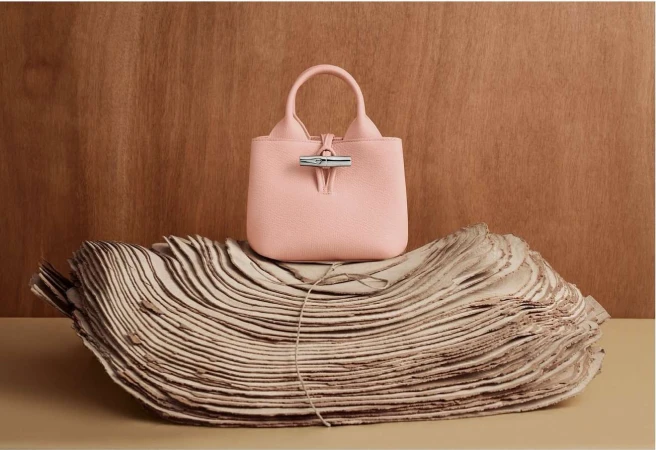 Stylish pink leather handbag on sculpted paper against a wood backdrop. Fashion product shot with luxury feel, studio lighting, and clean style.