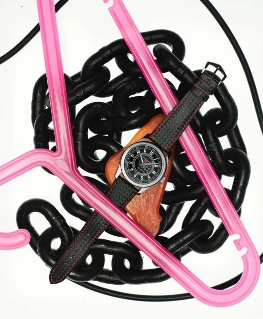 Wristwatch on a brown surface with black chains and pink plastic hangers against a white backdrop in a studio setting.