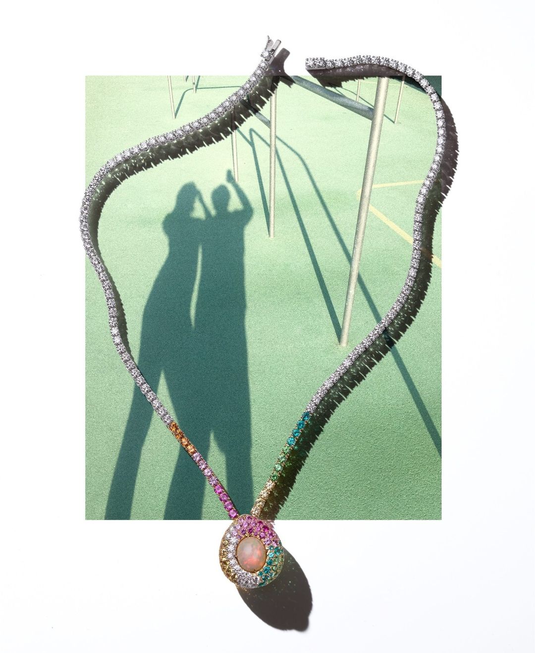 Elegant diamond necklace with rainbow gemstones on a green surface, casting shadows of two people and a metal structure.