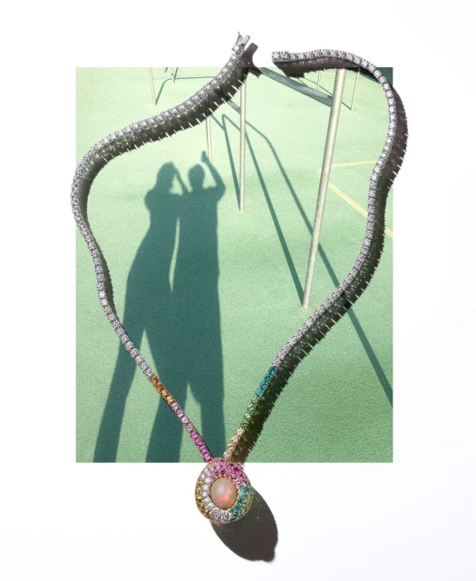 Elegant diamond necklace with rainbow gemstones on a green surface, casting shadows of two people and a metal structure.