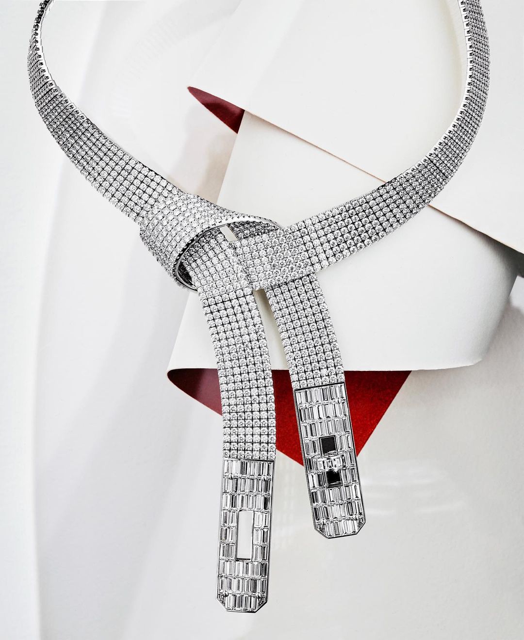 Elegant diamond necklace with tie-knot detail on a white surface with a hint of red creates a striking and luxurious jewelry piece.
