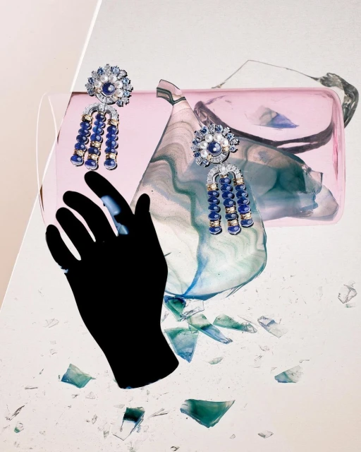 Still-life product shot of two ornate blue, white, and gold earrings on a shattered surface, a pink purse, and a black glove.