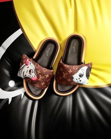 Two Louis Vuitton slides with cartoon animal embellishments placed against a vibrant yellow and black backdrop.