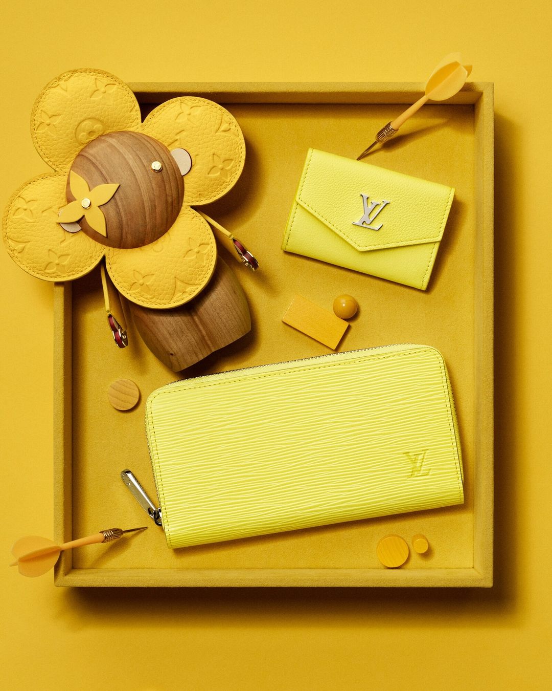 Still life of Louis Vuitton leather wallets and wooden flower sculpture on yellow backdrop, studio product shot, luxury fashion accessory.