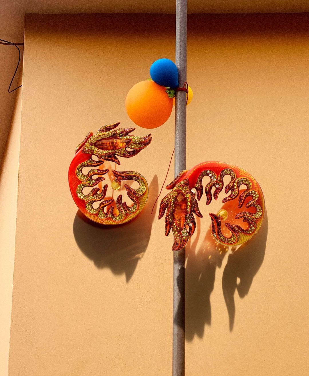 Wall decoration featuring two shrimp-shaped objects with orange and gold accents, attached to a pole with blue and orange ball ornaments.