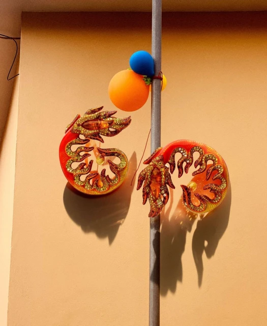 Wall decoration featuring two shrimp-shaped objects with orange and gold accents, attached to a pole with blue and orange ball ornaments.