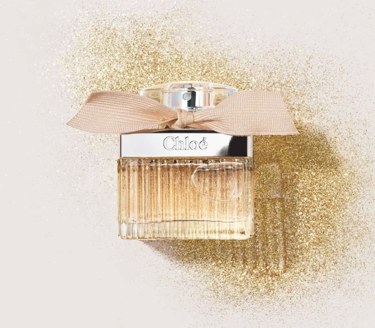 Close-up of a Chloe perfume bottle against a gold glitter background, showcasing luxury and elegance in a still-life composition.