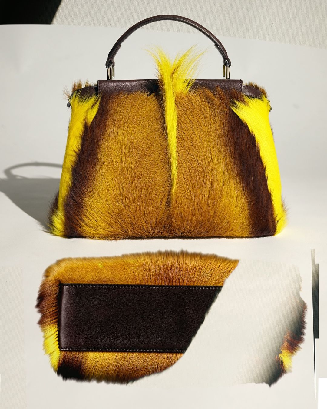 Fashionable brown and yellow fur handbag with a dark brown leather handle and bottom panel on a clean white surface. 