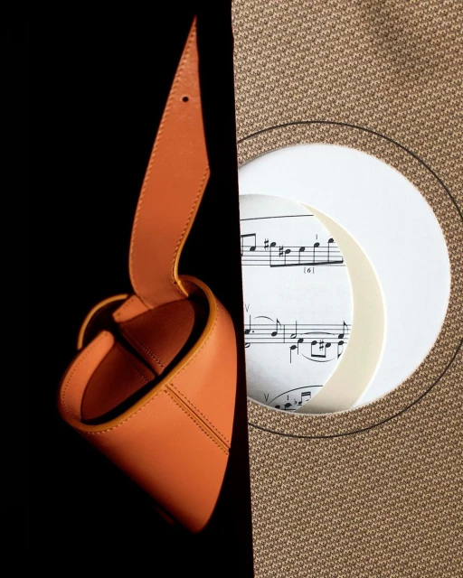 Leather bag and musical score. An artful composition combines a tan leather bag with sheet music and a tan woven background.