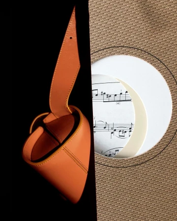 Leather bag and musical score. An artful composition combines a tan leather bag with sheet music and a tan woven background.