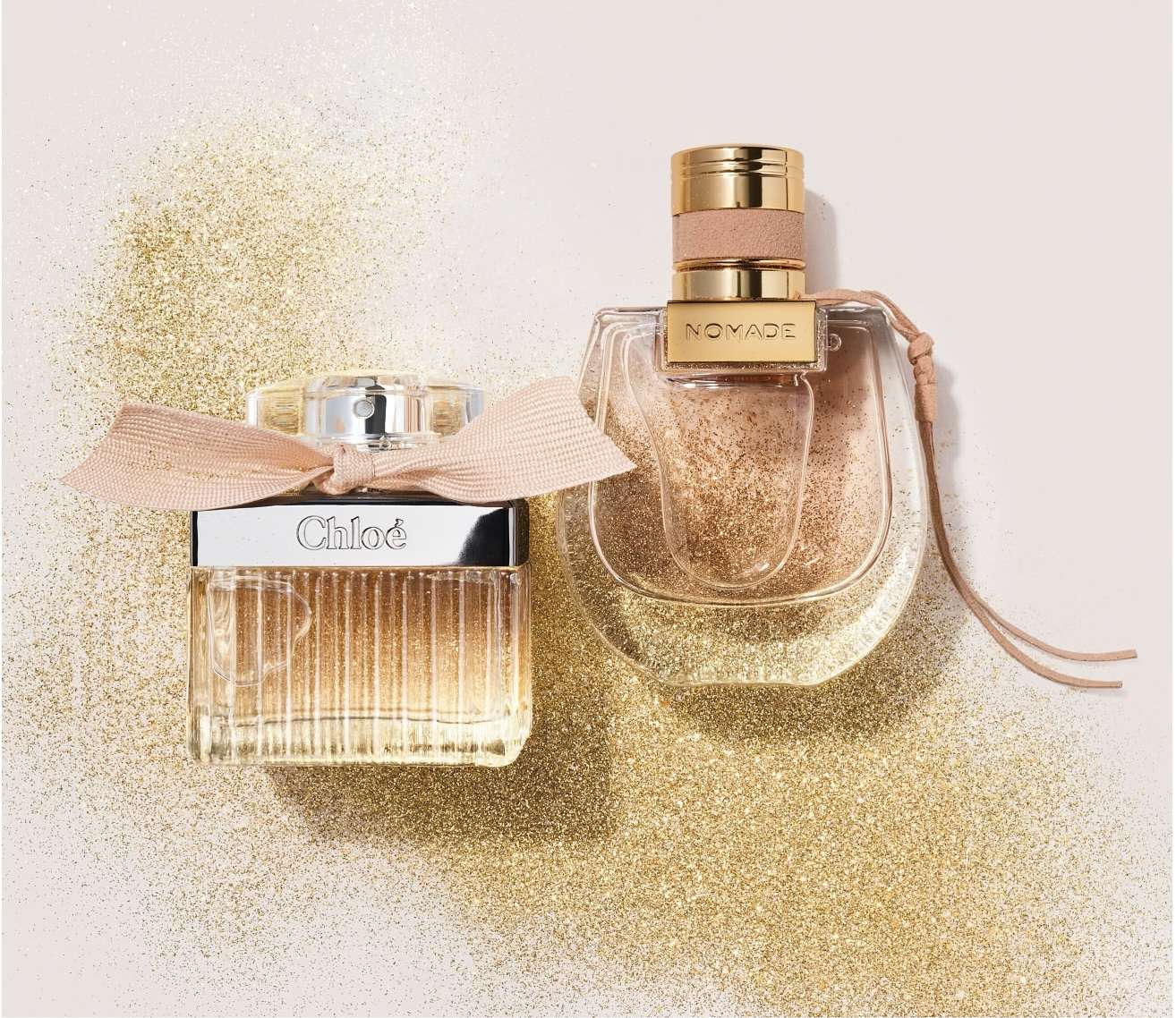 Two perfume bottles, Chloe and Nomade, sit on a sparkling gold surface. Chloe is rectangular with a bow, while Nomade is curved.