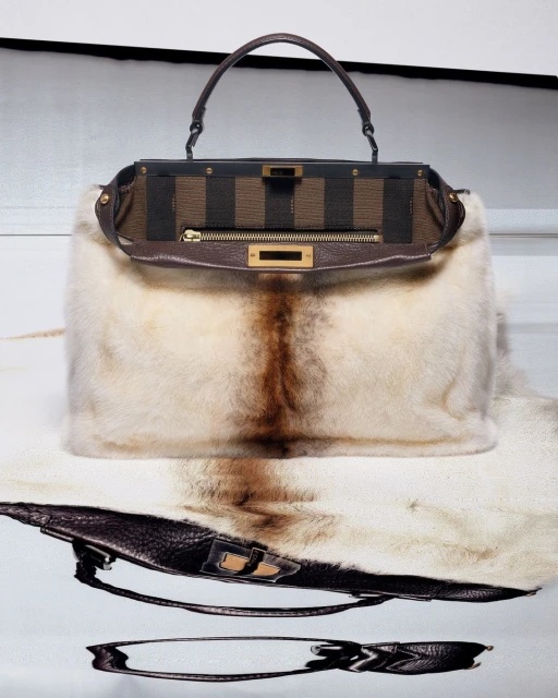Luxurious Fendi Peekaboo handbag in beige fur and brown striped fabric, showcased on a fur surface against a clean white backdrop.