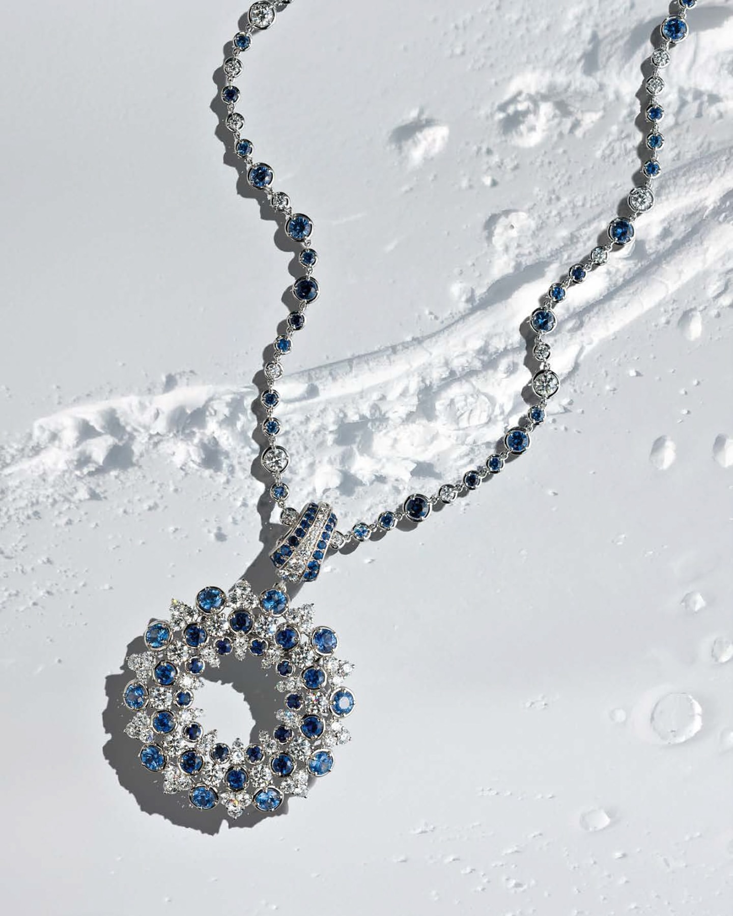 Elegant necklace with blue and white gemstones displayed on a textured white surface in a high-angle product shot for jewelry design.