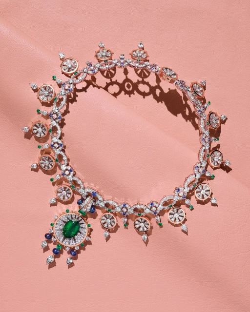 Elegant necklace with emerald, sapphire, and diamond gemstones against a pink leather backdrop. Jewelry design for fashion and beauty.