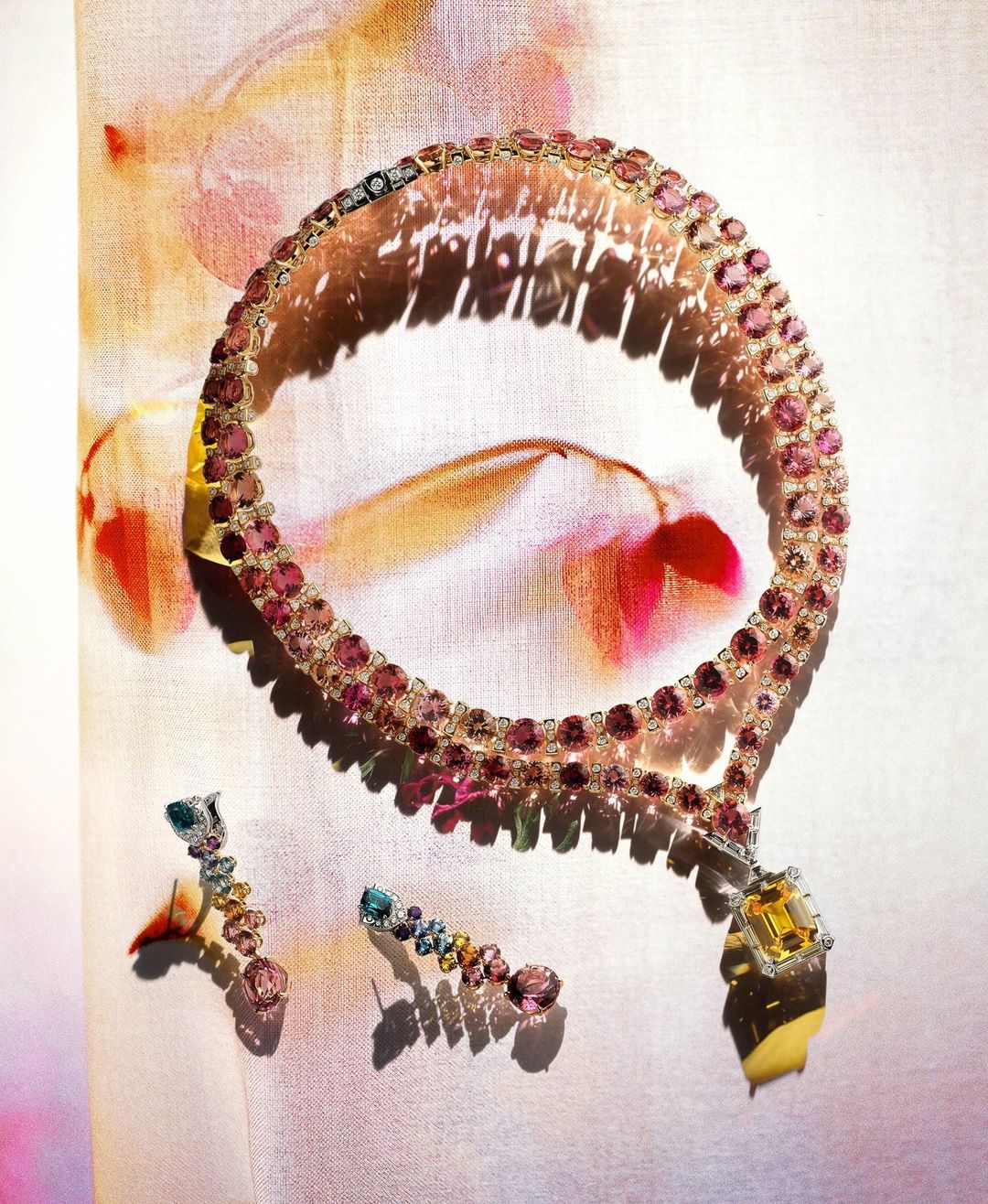 Elegant gemstone jewelry: A pink and yellow gem-studded necklace with matching earrings displayed on a textured floral background.
