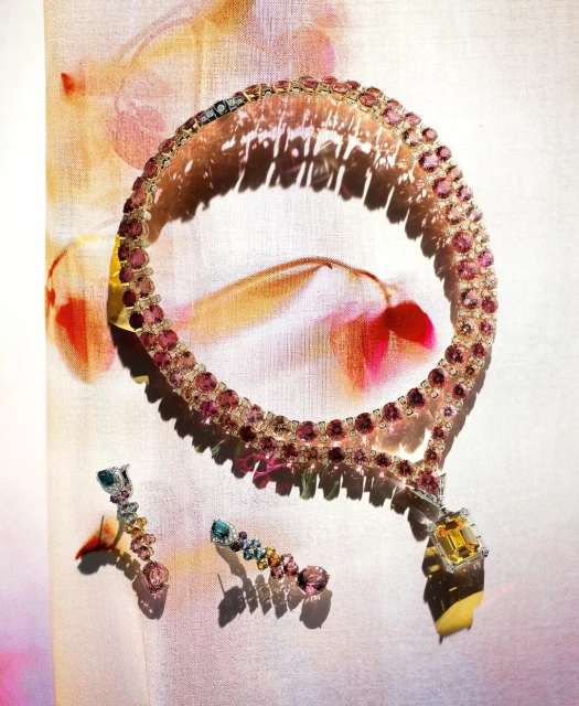 Elegant gemstone jewelry: A pink and yellow gem-studded necklace with matching earrings displayed on a textured floral background.