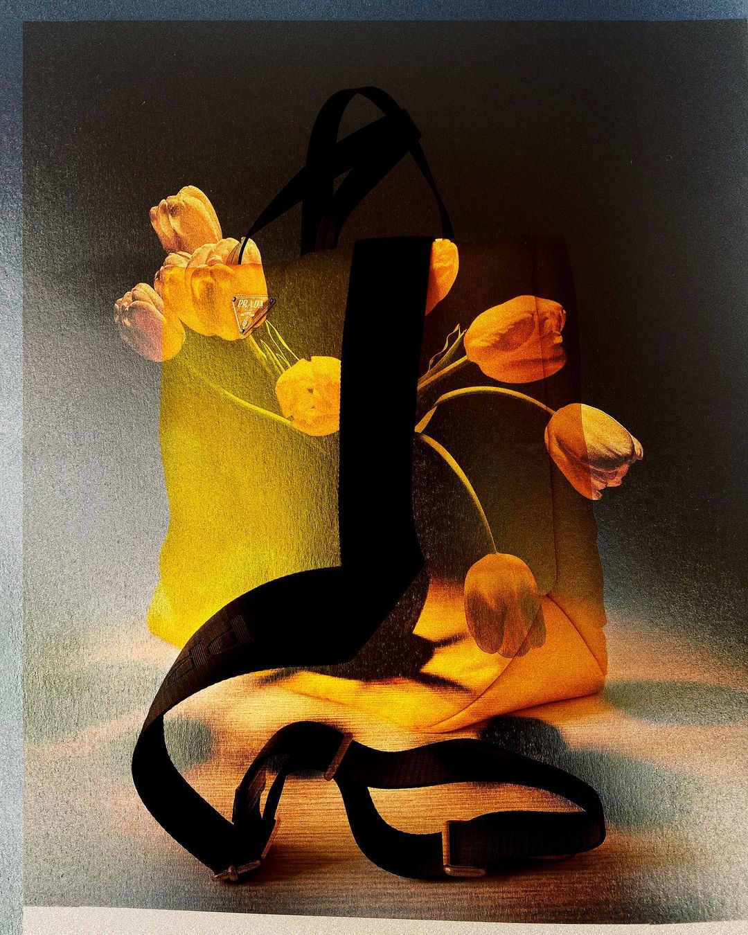 Still life featuring a yellow tote bag with black straps, adorned with orange tulip flowers, set against a textured studio backdrop.