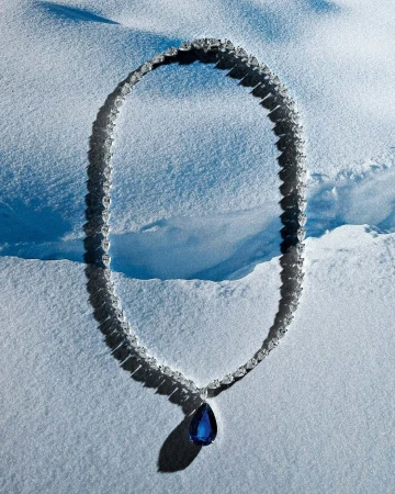 Elegant diamond necklace with teardrop sapphire pendant displayed on a snowy surface, highlighting luxury and natural contrast.