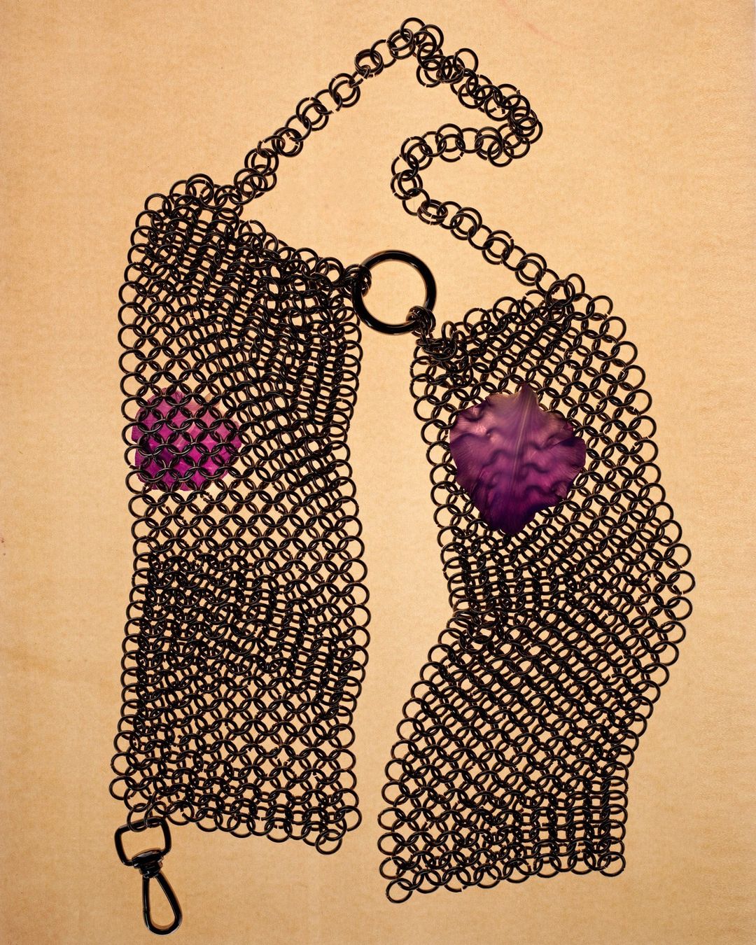 Black chainmail necklace with two purple gemstone embellishments on a light beige surface. Jewellery fashion product shot.