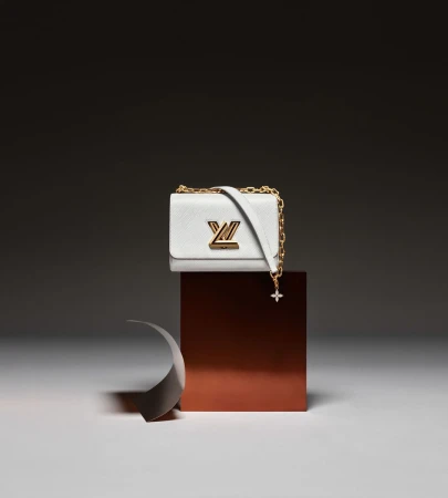 White leather Louis Vuitton purse with gold logo on a reflective brown block against a grey background, studio shot.