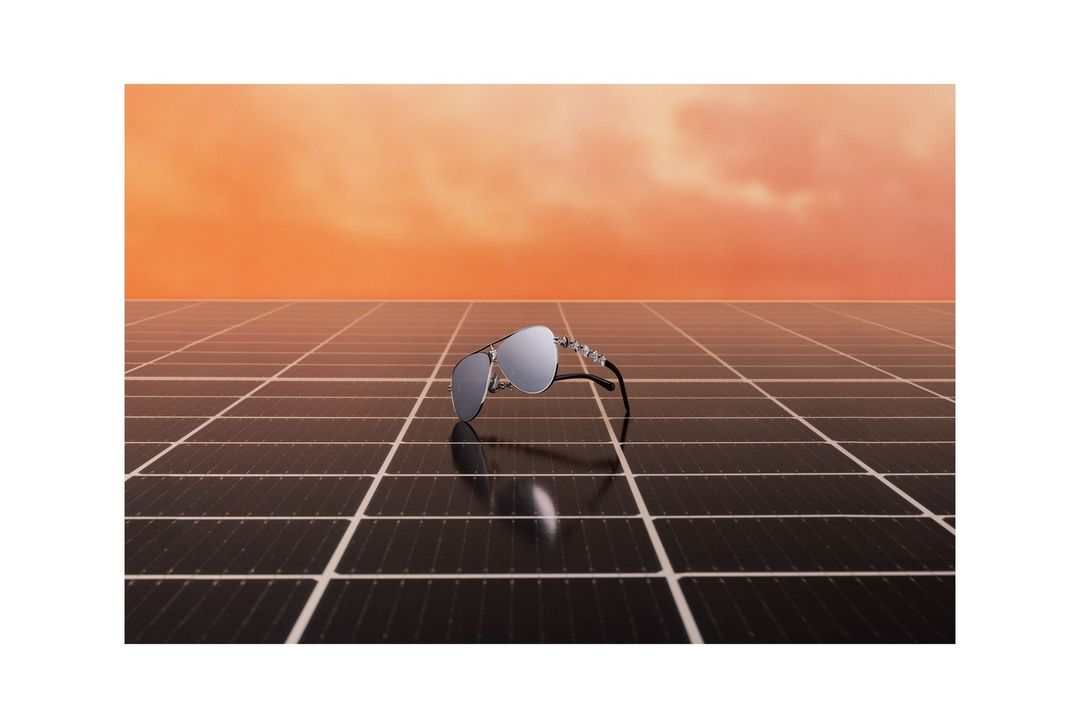 Aviator sunglasses on a solar panel against an orange sky. The reflective lenses mirror the landscape, creating a modern still life.