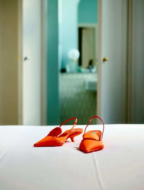 Elegant pair of pointed orange slingback heels showcased on a pristine white surface, bathed in soft lighting against a blurred background.