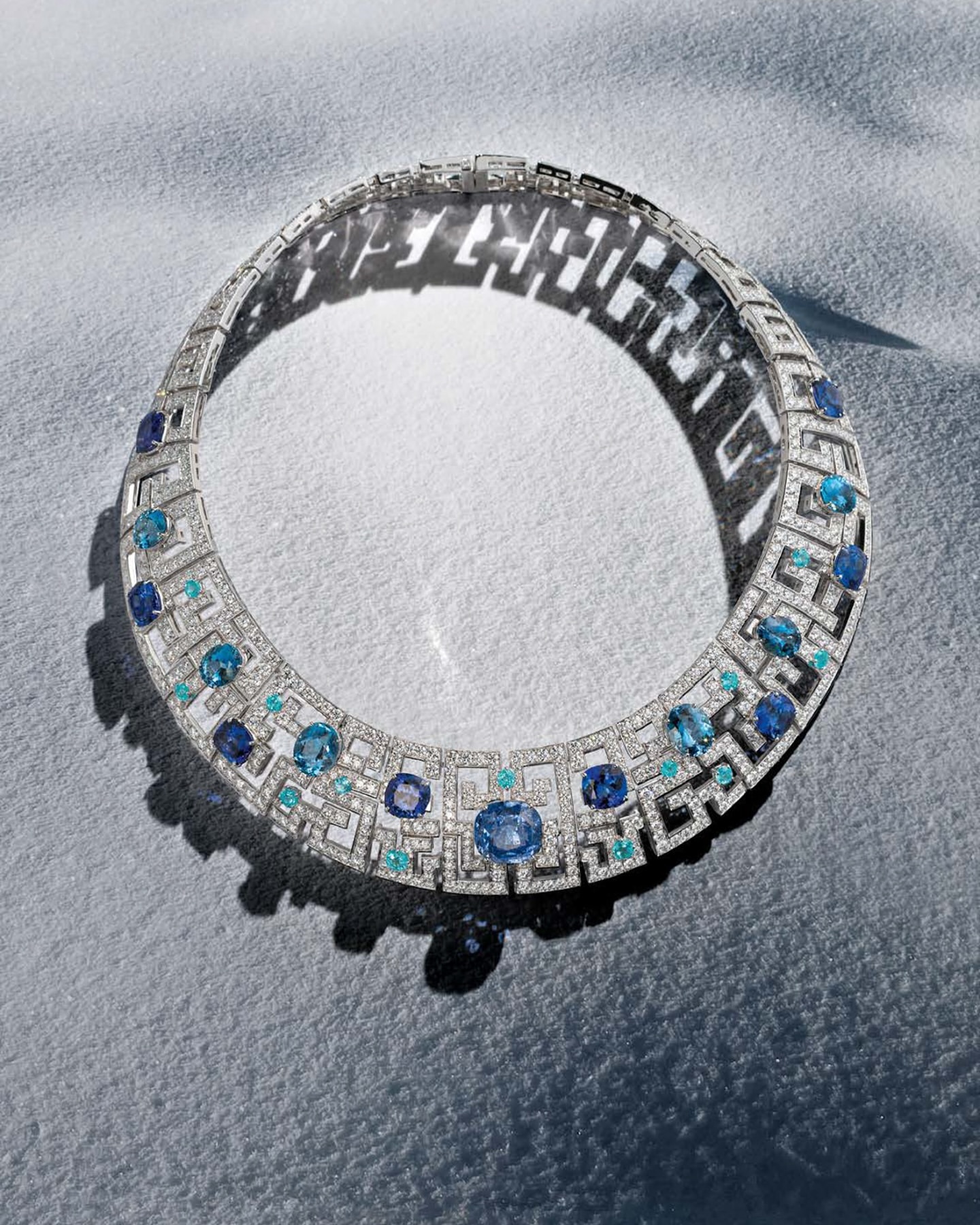 Overhead studio shot of a diamond and sapphire necklace, displaying intricate geometric details and a bright, luxurious aesthetic.