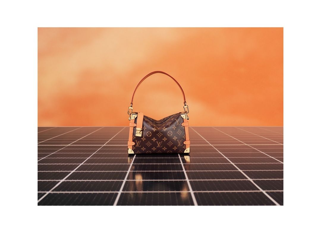 Luxury Louis Vuitton handbag with a monogram pattern on a black solar panel grid against a peach-toned background, fashion studio shot.