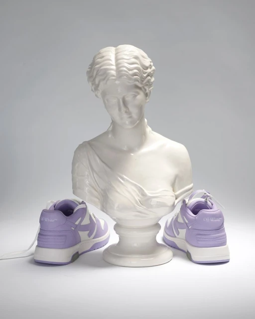 Still life shot of lavender and white sneakers flanking a Greco-Roman style bust on a neutral background. Fashion footwear.