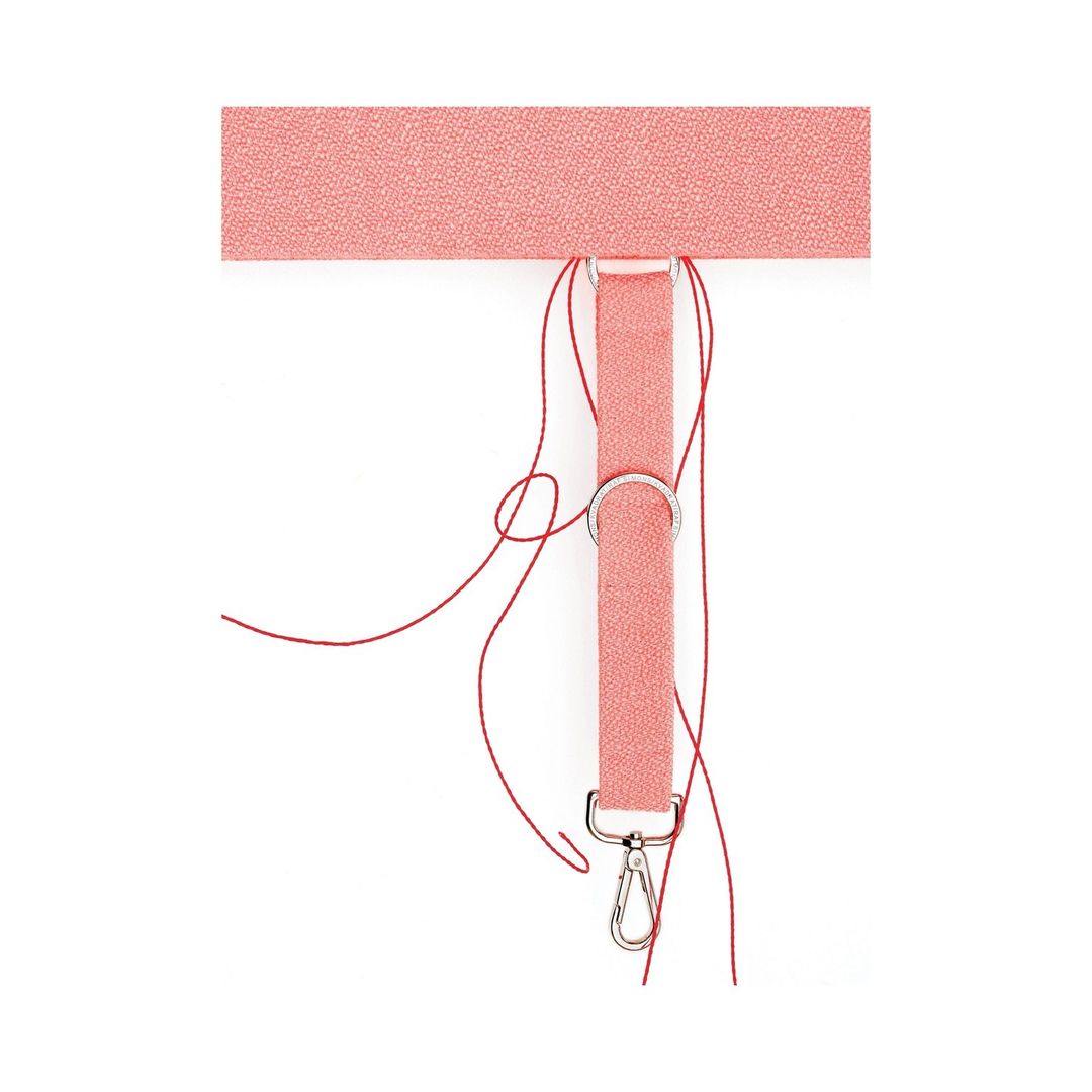 Close-up of a textured pink strap with metal rings, a clip, and loose red threads against a clean white background, studio shot.