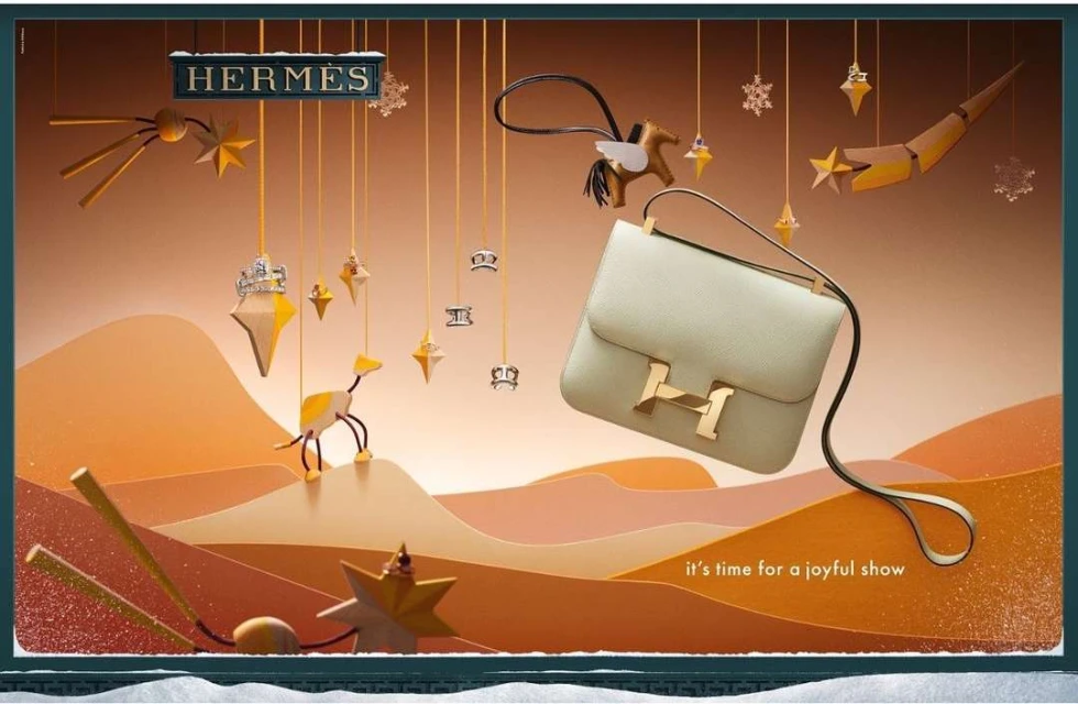 Hermès handbag with a horse bag charm, decorative stars and shapes, warm lighting, and paper-cut landscape in a window display.