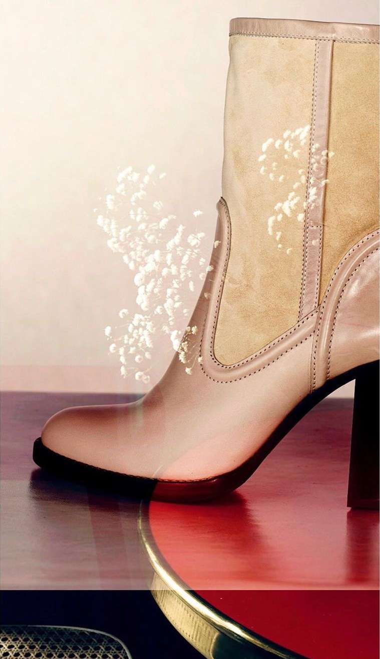 Beige leather ankle boot with a block heel against a neutral gradient background with glitter-like bokeh, reflecting on a red surface.