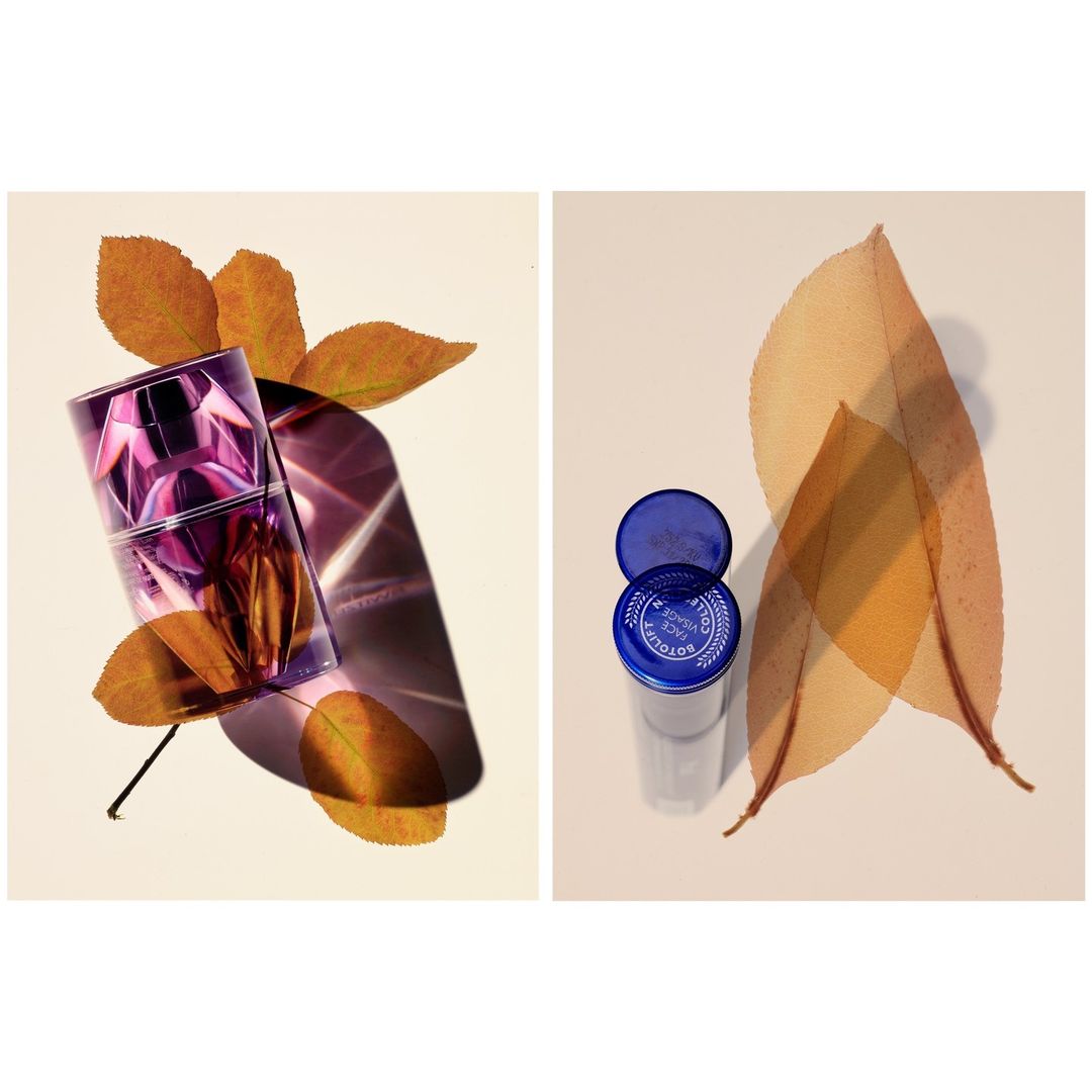Purple perfume bottle displayed with orange leaves, adjacent to a transparent container with a blue lid and leaves.