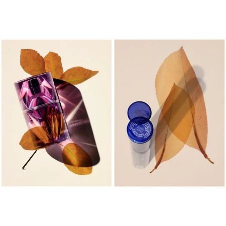 Purple perfume bottle displayed with orange leaves, adjacent to a transparent container with a blue lid and leaves.