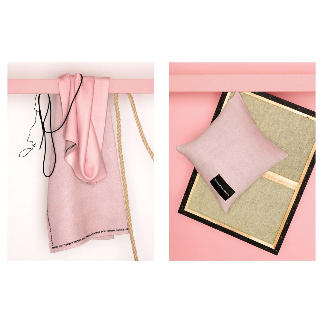 Stylized studio shot of a pink towel and a pillow on a pink shelf with pink background, paired with ropes and a framed artwork.