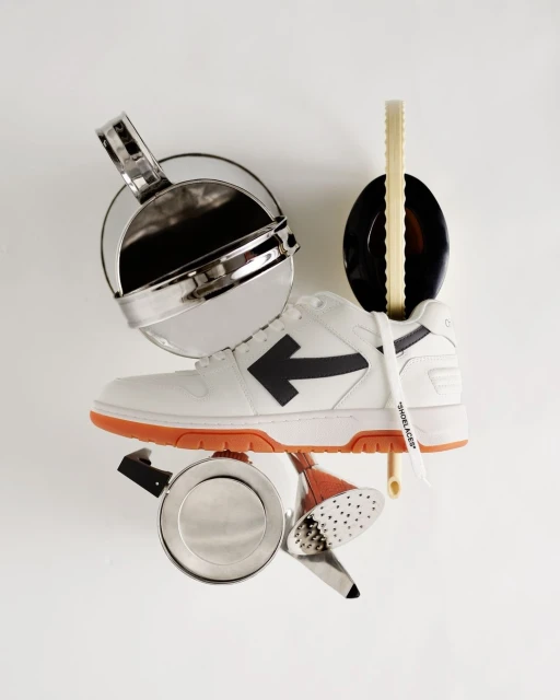 Studio shot of a white and orange Off-White sneaker surrounded by various silver kitchen objects against a white background.