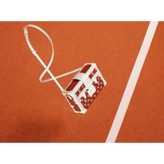 Red and white Louis Vuitton purse with strap, angled on a tennis court surface with white lines, studio shot.