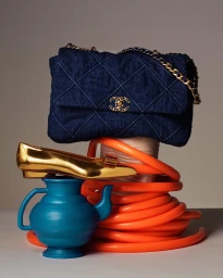 Quilted blue denim handbag resting on a coiled orange tube with a metallic gold shoe and a blue ceramic teapot.