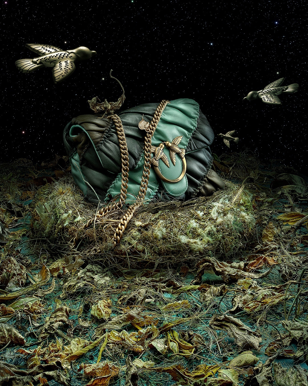 Close-up of a teal and black quilted leather handbag with a gold chain strap, sitting on dried leaves, surrounded by birds against a starry sky.