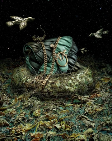 Close-up of a teal and black quilted leather handbag with a gold chain strap, sitting on dried leaves, surrounded by birds against a starry sky.