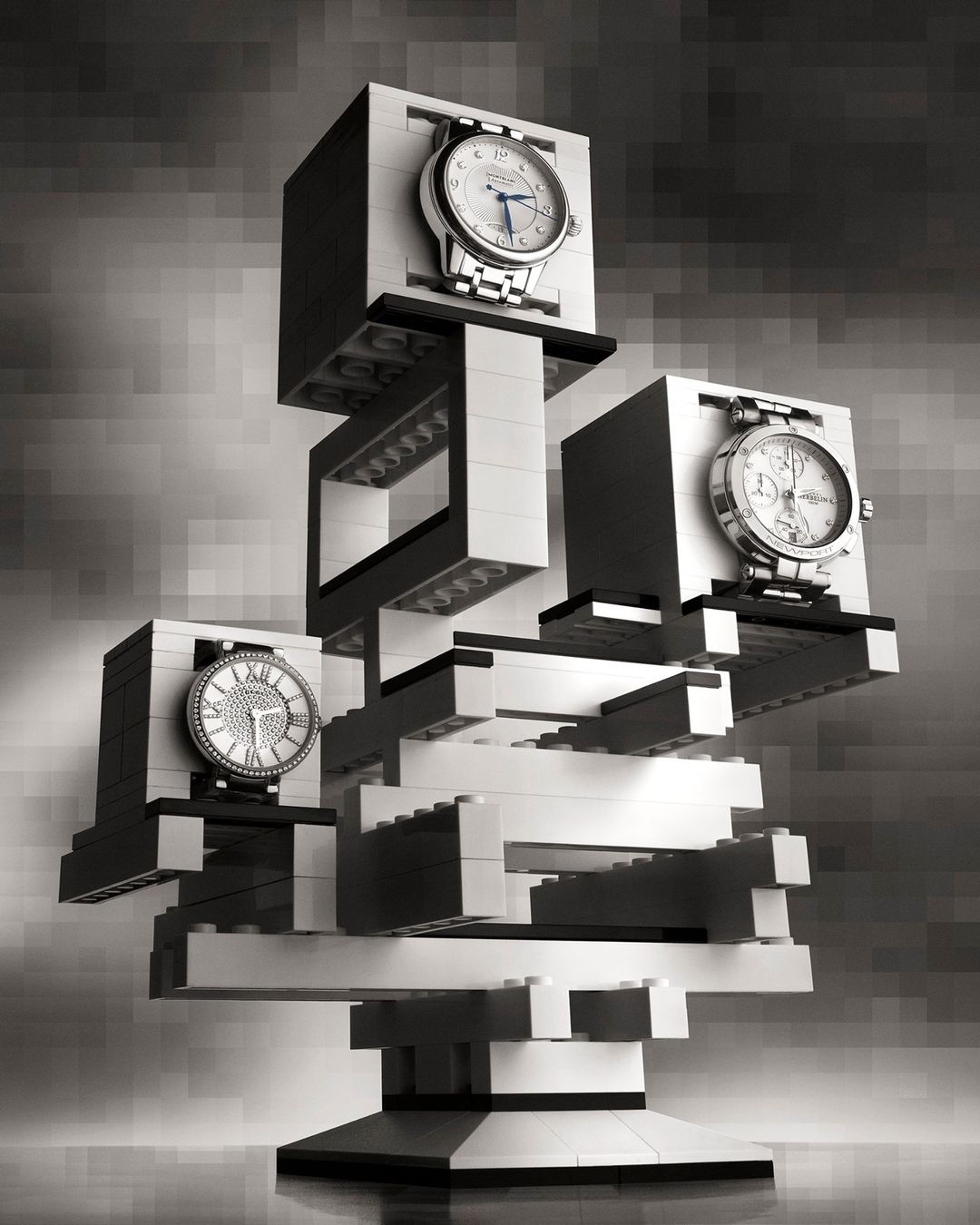 Three silver wristwatches are displayed on a sculpture made of grey and white toy building blocks in a studio setting.
